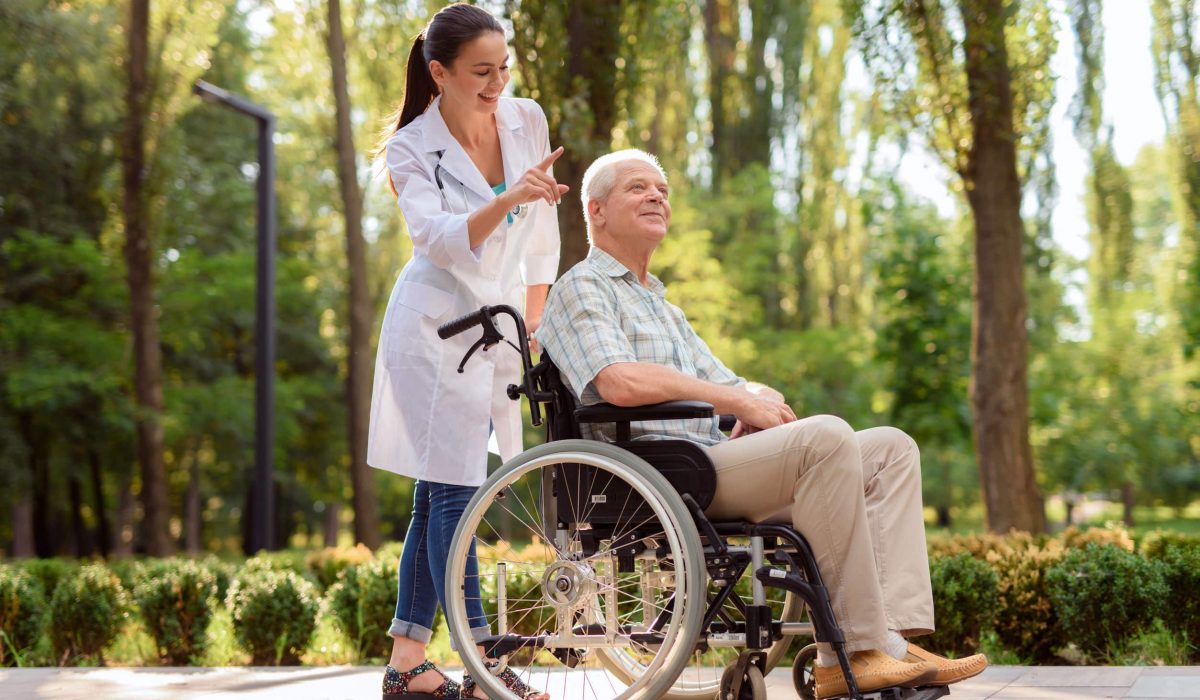 Happy old man in wheelchair in park with doctor