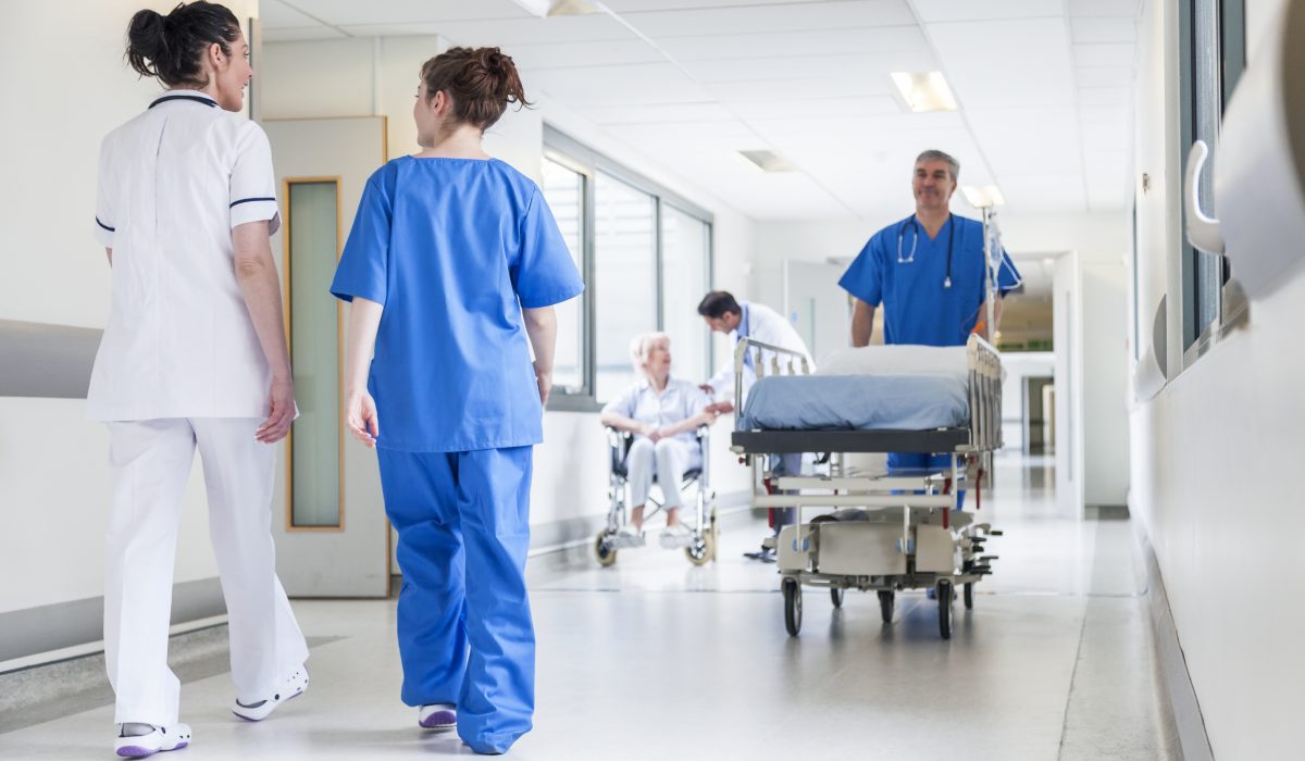 Male nurse pushing stretcher gurney bed in hospital corridor with doctors & senior female patient